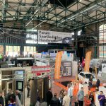 Menschen erkunden verschiedene Stände auf einer überdachten Messe, über denen Banner mit der Aufschrift Forum Saarländisches Handwerk hängen. Der Veranstaltungsort hat hohe Decken, große Fenster und Aussteller, die ihre Produkte und Dienstleistungen vorstellen.